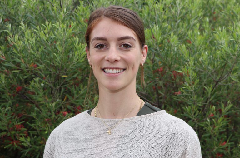 Portrait of a smiling woman in white sweater with green plants in the background