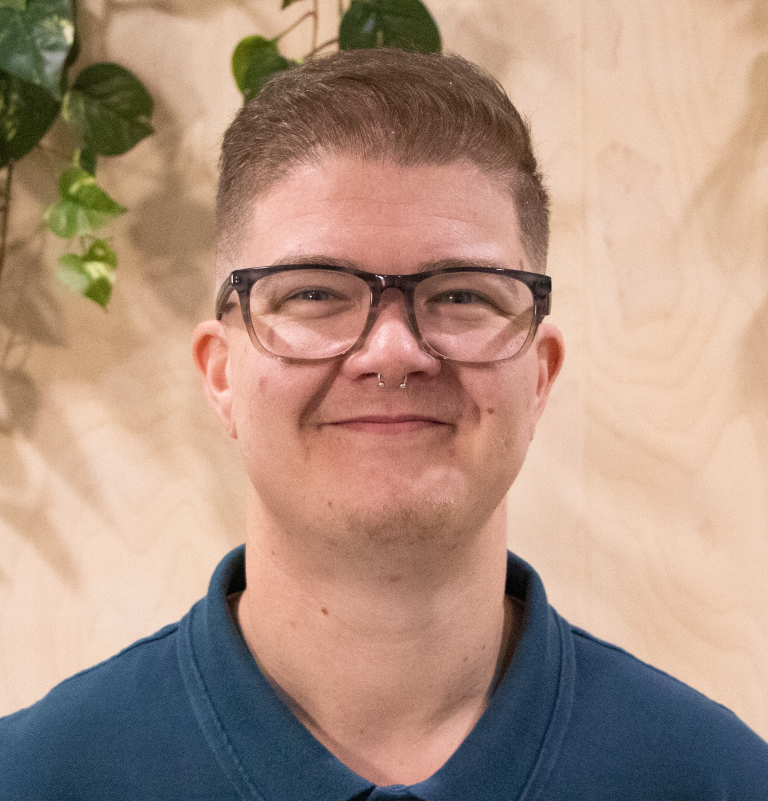 A smiling person in front of leafy plants.