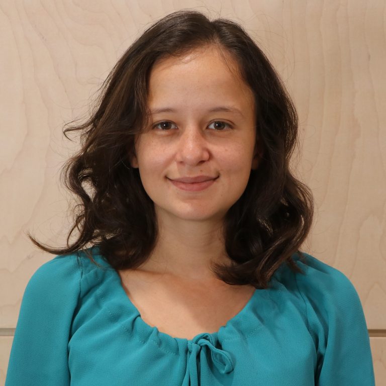 A woman with curly hair wearing a teal blouse, smiling at the camera.