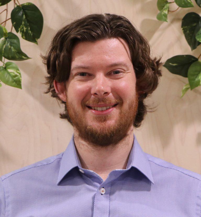 Smiling individual with curly hair and greenery background.