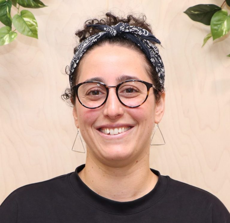 Smiling curly hair person with triangle earings in a modern setting.
