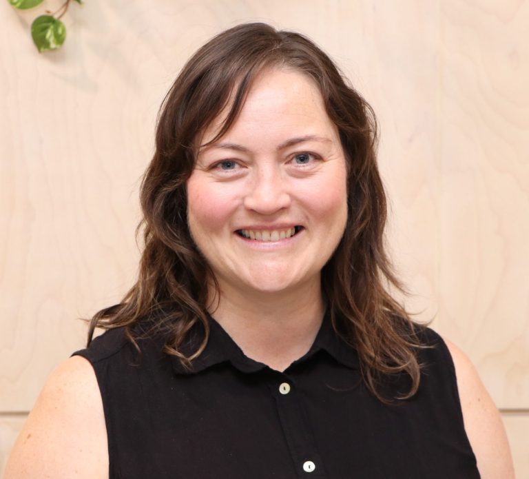 A portrait of a smiling person with brown hair and a black shirt.