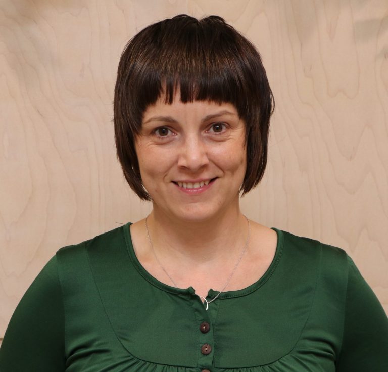 A short hair woman smiling while wearing a green shirt.