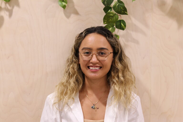 A woman with curly hair wearing a white suit, smiling at the camera.