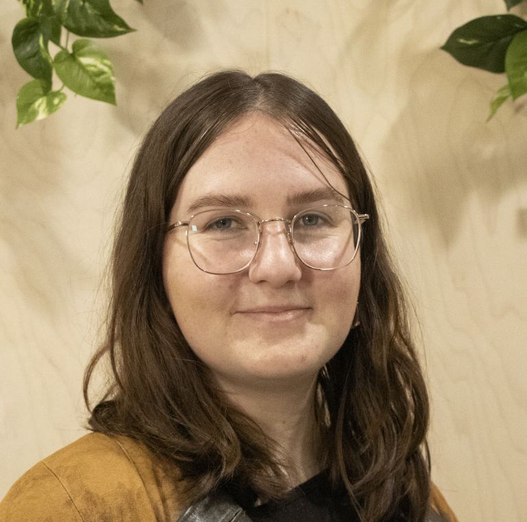 A smiling person using glasses with plants in the background, captured in a warm environment.