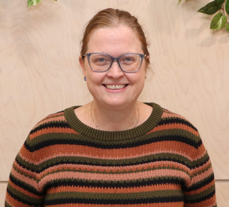 A woman is smiling while wearing a colorful striped sweater.