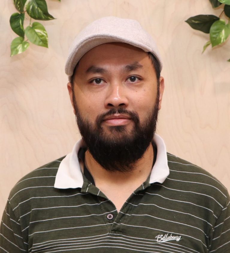 Portrait of a man with a beard and cap, surrounded by indoor plants.